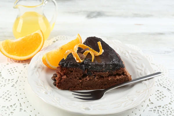 Pedazo de pastel de chocolate y naranja en el plato, sobre el fondo de la mesa — Foto de Stock