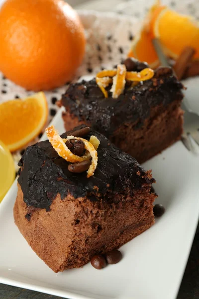 Porción de pastel con glaseado de chocolate y naranja en plato, sobre fondo de madera — Foto de Stock