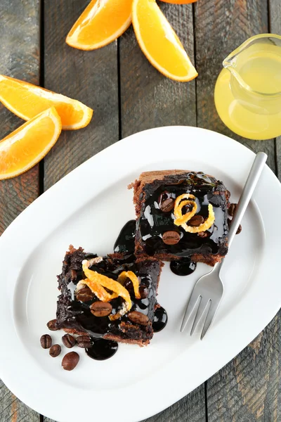 Gedeelte van Cake met chocolade glazuur en oranje op plaat, op houten achtergrond — Stockfoto