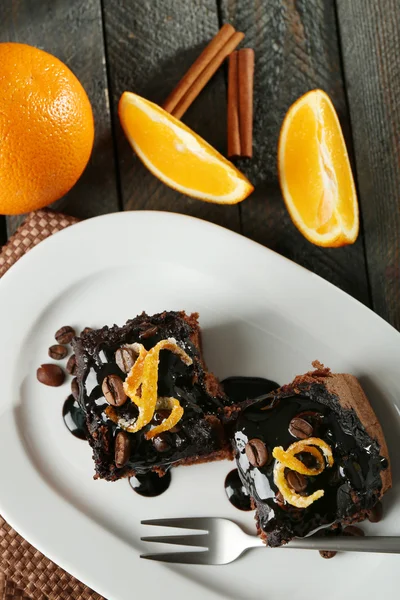 Porción de pastel con glaseado de chocolate y naranja en plato, sobre fondo de madera — Foto de Stock