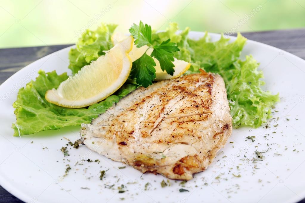 Dish of fish fillet with lettuce and lemon on table close up