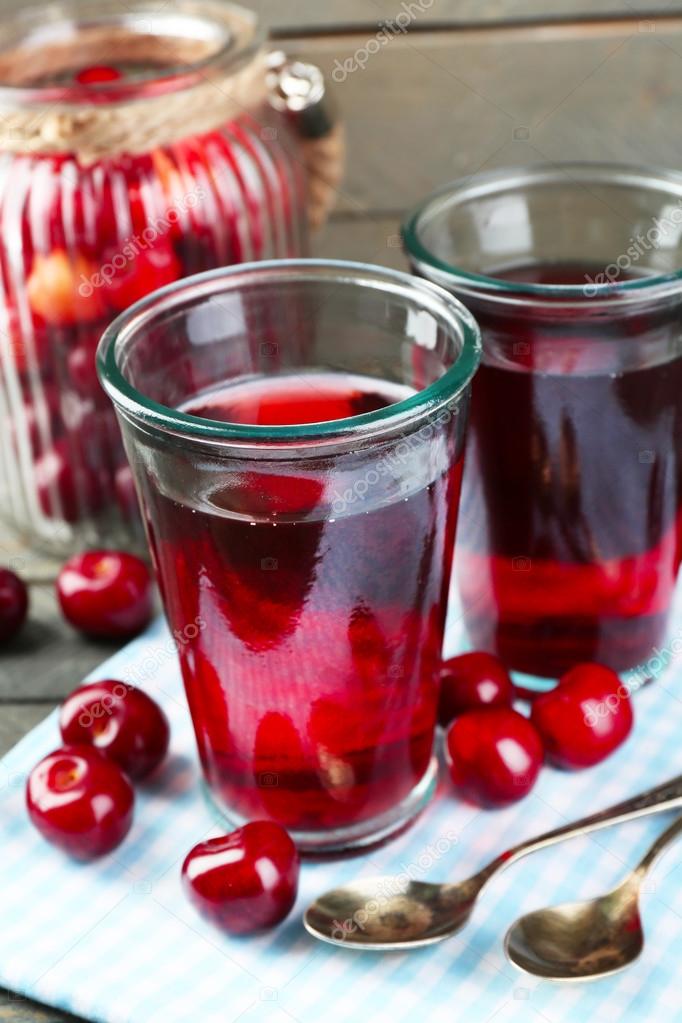 Glasses of sweet homemade cherry compote on table on wooden background