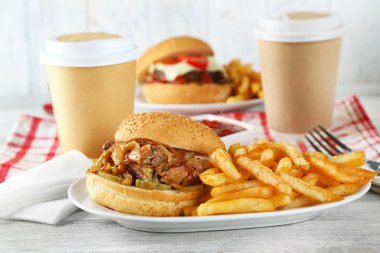 Lezzetli hamburger ve patates kızartması tabakta, ahşap masa arkasında. Sağlıksız gıda konsepti
