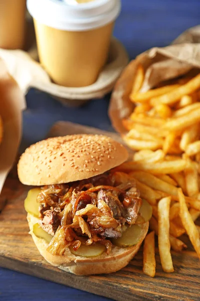 Вкусный бургер и картофель фри на тарелке, на деревянном фоне стола. Концепция нездорового питания — стоковое фото
