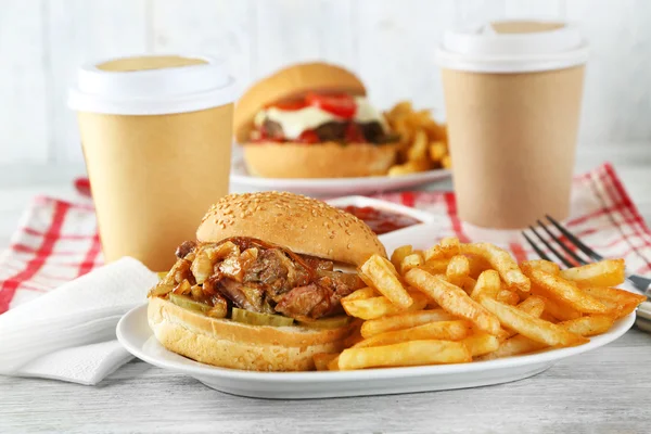 Вкусный бургер и картофель фри на тарелке, на деревянном фоне стола. Концепция нездорового питания — стоковое фото