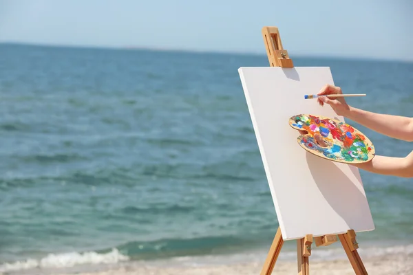 Палитра для женских рук с красками и мольбертом на пляже — стоковое фото