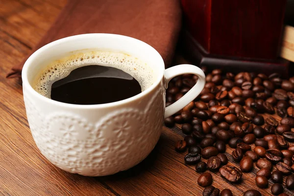 Kopje verse koffie met bonen op tafel, close-up — Stockfoto