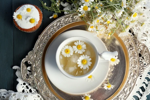 Xícara de chá de camomila com flores de camomila e queques saborosos na bandeja, na cor de fundo de madeira — Fotografia de Stock