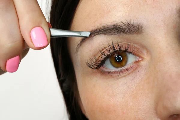 Young woman plucking eyebrows with tweezers close up — Stock Photo, Image