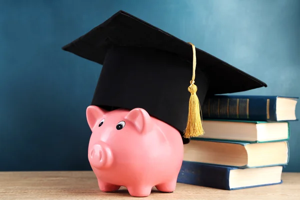 Piggy bank met boeken en Grad hoed op blackboard achtergrond — Stockfoto
