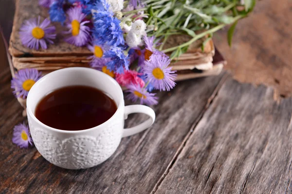 Libros antiguos con hermosas flores y taza de té en la mesa de madera de cerca — Foto de Stock