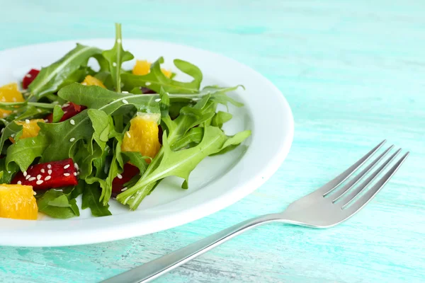 Insalata saporita con foglie di rucola in piatto su tavolo di legno, primo piano — Foto Stock