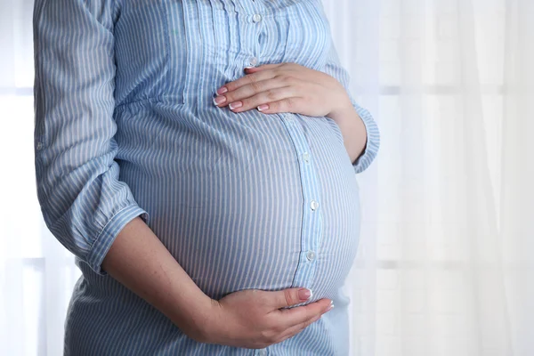 Bella giovane donna incinta toccare la pancia su sfondo chiaro — Foto Stock