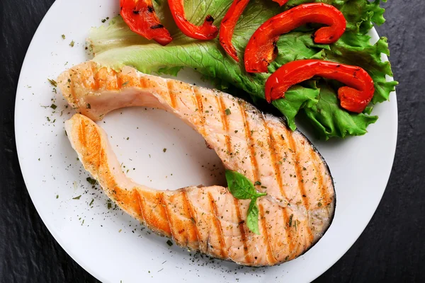 Sabroso salmón a la parrilla con ensalada de pimienta y lechuga en la mesa de cerca — Foto de Stock