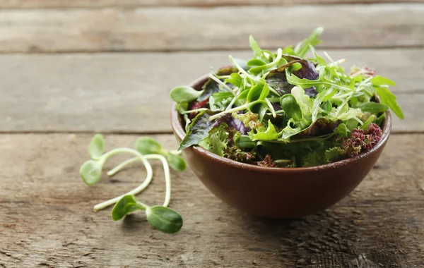 Fresh mixed green salad in bowl on wooden table close up — Stock Photo, Image