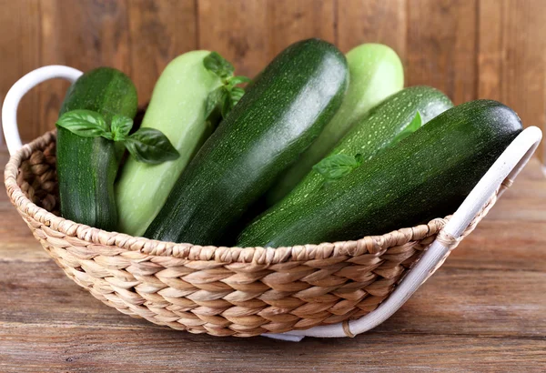 Cukety s squash a bazalkou v proutěném koši na dřevěné pozadí — Stock fotografie