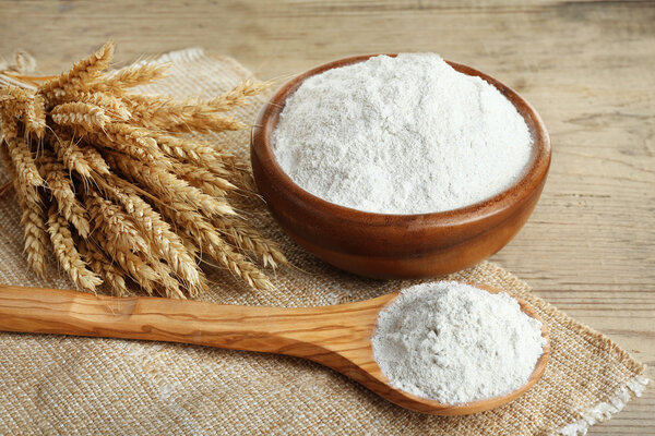 Целая мука в миске с пшеничными ушами на деревянном столе, крупным планом
