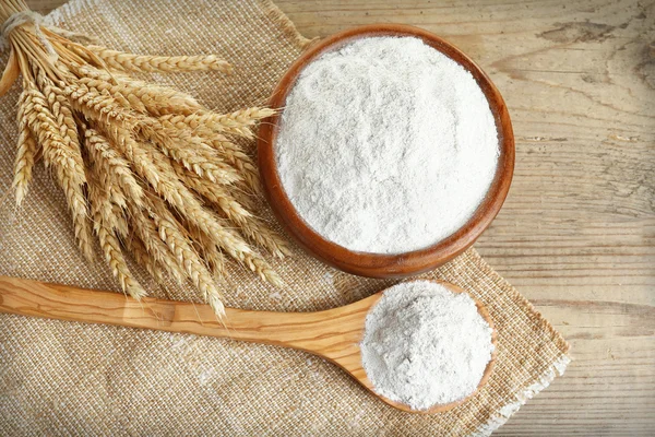 Whole flour in bowl with wheat ears on wooden table, top view — Stock Photo, Image