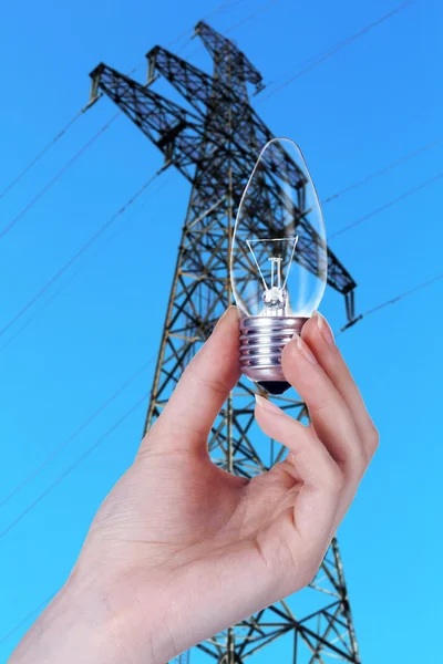 Glühbirne in der Hand auf Hochspannungsleitung Hintergrund — Stockfoto