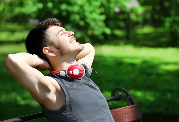 Uomo con cuffie poggiate su panchina nel parco — Foto Stock