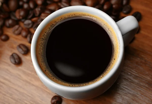 Tazza di caffè fresco con fagioli sul tavolo, primo piano — Foto Stock