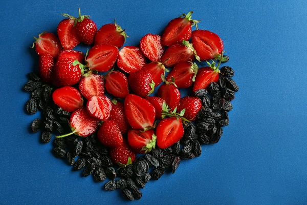 Strawberry and prunes in shape of heart on blue background — Stock Photo, Image