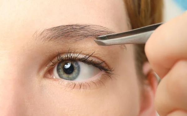 Mujer joven arrancando las cejas con pinzas de cerca —  Fotos de Stock