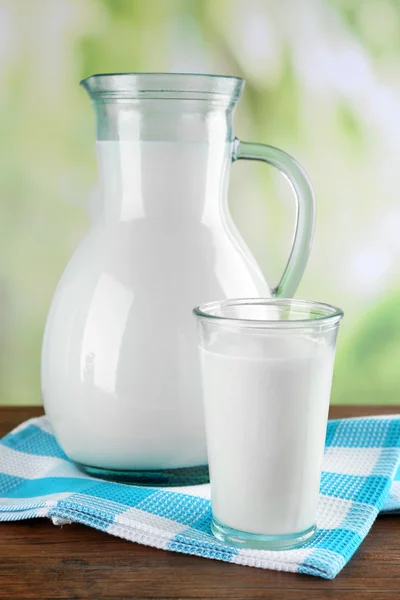 Brocca e bicchiere di latte sul tavolo di legno, sullo sfondo della natura — Foto Stock