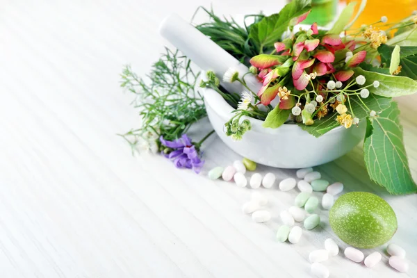 Herbes au mortier, éprouvettes et pilules, sur table, sur fond clair — Photo