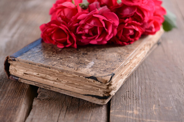 Old book with beautiful roses on wooden table close up