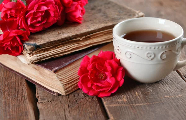 Old books with beautiful flowers and cup of tea on wooden table close up — Stock Photo, Image