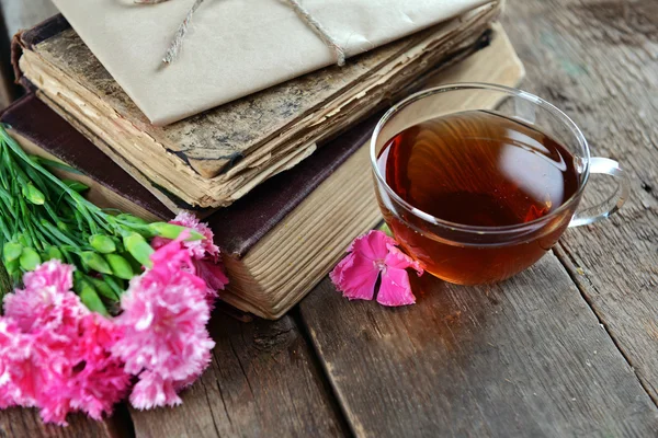 Gamla böcker med vackra blommor och kopp te på träbord nära håll — Stockfoto