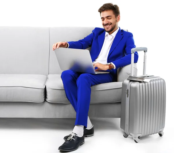 Hombre de negocios con maleta y portátil sentado en el sofá aislado en blanco — Foto de Stock