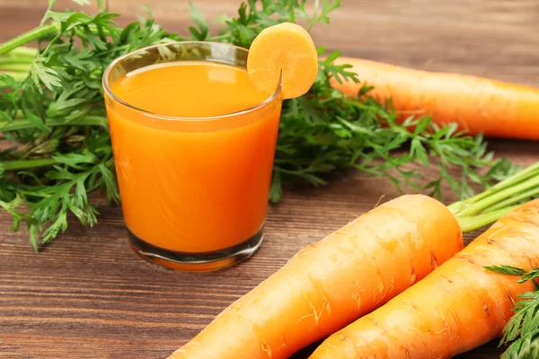 Se acercan los vasos del jugo de zanahoria con hortalizas a la mesa —  Fotos de Stock