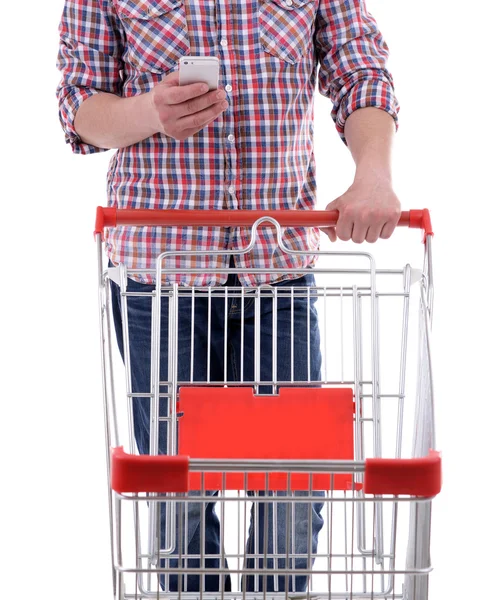 Young man holding mobile phone and shopping cart isolated on white — Stock Photo, Image