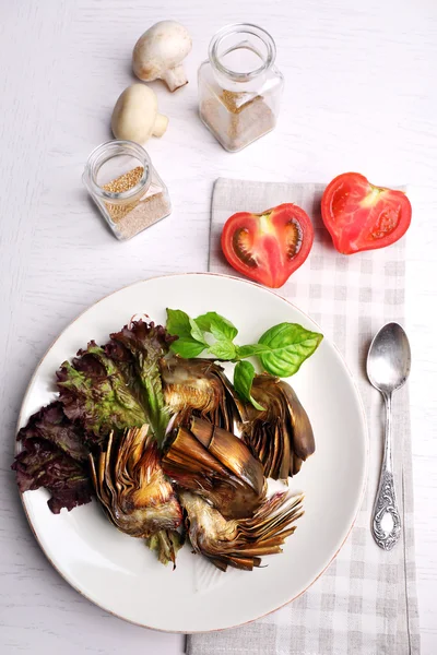 Roasted artichokes on plate, on kitchen table background — Stock Photo, Image