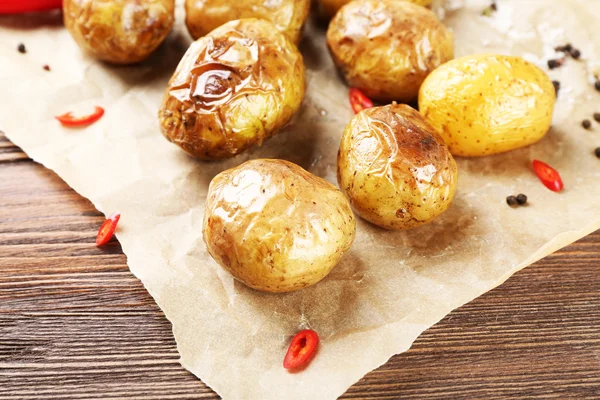 Gebakken pittige aardappelen op perkament op houten tafel, close-up — Stockfoto