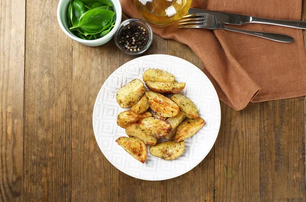 Pommes de terre épicées cuites au four dans une assiette blanche sur une table en bois, vue de dessus — Photo