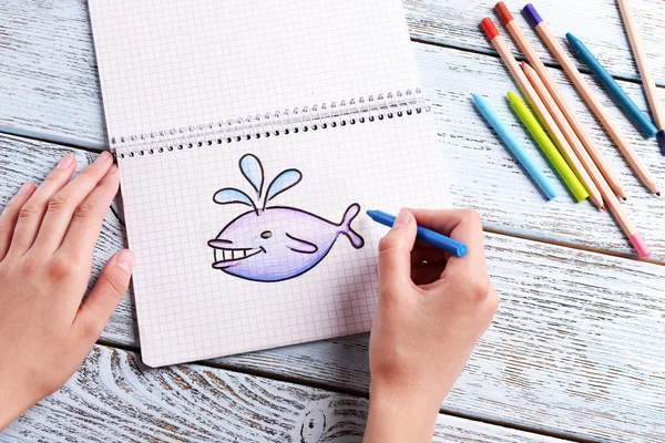 Női kezek bálna rajz notebook, fából készült asztal háttér — Stock Fotó