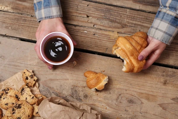 Female hands holding cup of coffee and cookies on wooden table close up — Stock Photo, Image