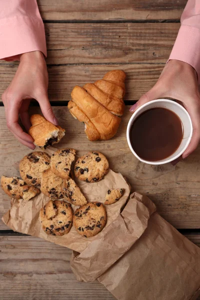 Female hands holding cup of coffee and cookies on wooden table close up — Stock Photo, Image