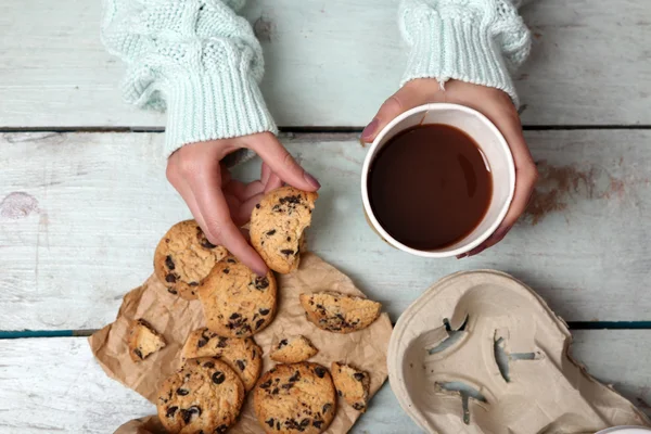 Female hands holding cup of coffee and cookies on wooden table close up — Stock Photo, Image