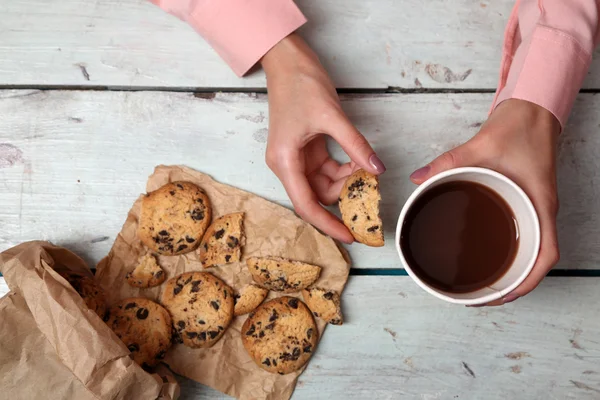 Frauenhände halten Tasse Kaffee und Kekse auf Holztisch in Großaufnahme — Stockfoto