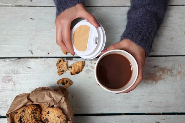 Frauenhände halten Tasse Kaffee und Kekse auf Holztisch in Großaufnahme — Stockfoto