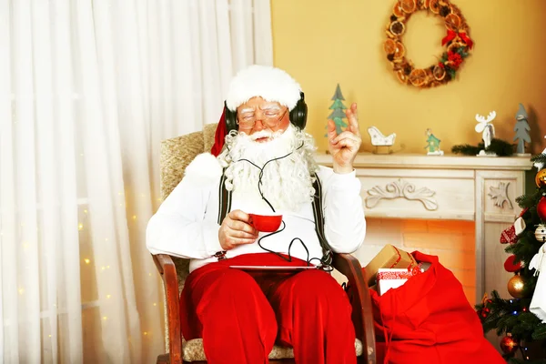 Noel Baba ile dijital tablet yakınındaki şömine evde rahat sandalyede oturmak — Stok fotoğraf
