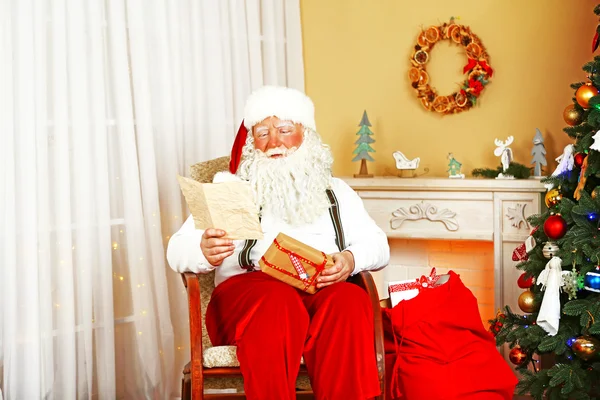 Santa claus siedzi z listy dzieci w wygodnym fotelu w pobliżu kominek w domu — Zdjęcie stockowe