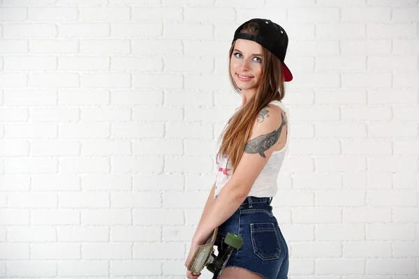 Menina hipster bonita com skate no fundo claro — Fotografia de Stock