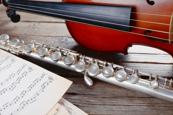 Flute and violin with music notes on wooden table close up — Stock Photo, Image