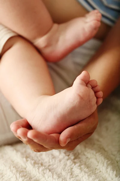 Volwassen handen houden de voeten van de baby, close-up — Stockfoto