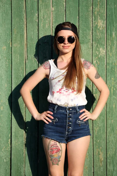 Beautiful girl with tattooed body, holding skateboard on wooden wall background — Stock Photo, Image